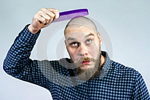 Portrait of sad bearded bald man hold comb in his hand. The concept of hair loss and hair transplantation