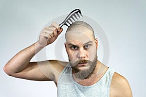 Portrait of sad bearded bald man holding a comb in his hand. The concept of hair loss and hair transplantation