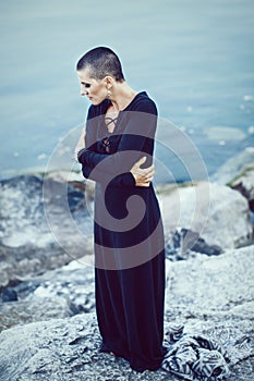 Portrait of sad beautiful Caucasian white young bald girl woman with shaved hair head standing by water lake looking away