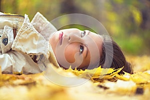 Portrait of sad beautiful young woman lying on the ground of an autumn forest with colorful maple leaves. Concept.