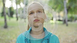 Portrait of sad blond girl looking at the camera and talking. Pretty caucasian teen complaining in the sunny park.