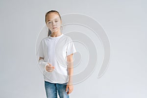 Portrait of sad blonde little girl with broken hand wrapped in white plaster bandage standing on white isolated