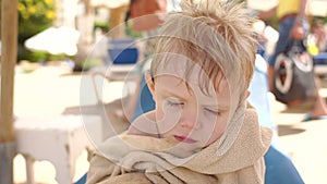 Portrait of a sad boy in beach towel by the pool.