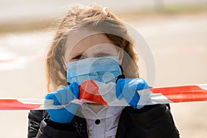 Portrait of sad caucasian child in face mask on closed playground outdoor. Coronavirus social distance quarantine