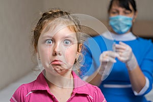 Portrait of a sad child on the background of a nurse in a medical mask. Little girl is afraid of vaccination. Kid does not want to