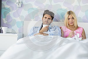 Portrait of sad couple holding coffee mug and glass while relaxing on bed