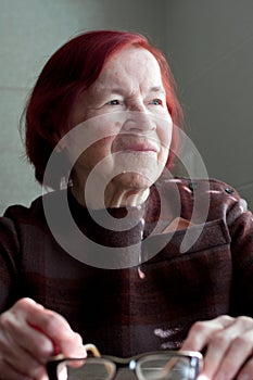 Portrait of sad elderly woman with red hair. Lonely grandmother looks out window and thinks about something.