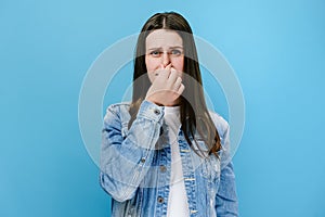 Portrait of sad emotional caucasian young woman feeling bad and dislike smell and hold nose from funny odor, wears denim jacket