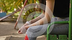 Portrait of a sad girl with dark hair sitting on the playground. Medium shot.
