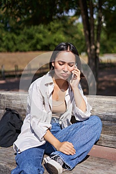 Portrait of sad girl talking on mobile phone and sulking. Young woman having an uneasy conversation on telephone