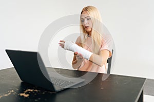 Portrait of sad injured young woman with broken arm wrapped in plaster bandage having video call, online consultation