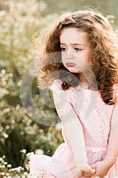 Portrait of a sad little curly girl in a pink long dress