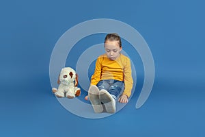 Portrait of sad little girl sitting on blue studio background, autism concept