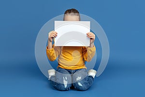 Portrait of sad little girl sitting on blue studio background, autism concept