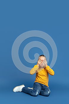 Portrait of sad little girl sitting on blue studio background, autism concept