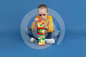 Portrait of sad little girl sitting on blue studio background, autism concept