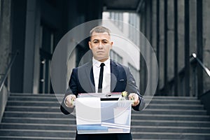 Portrait sad male office worker in depression with box of personal stuff. Businessman lost job. Fired man outdoors