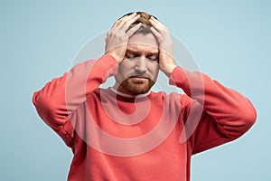 Portrait of sad man having life troubles holding head with suffering face on studio blue background.