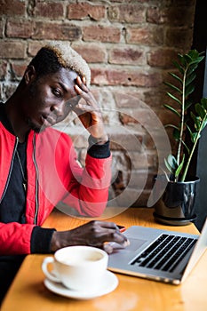 Portrait of sad man with a mobile phone sitting at cafe using laptop