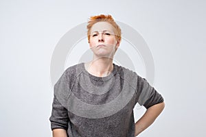 Portrait of a sad middle-aged woman with short red hair on a gray background.