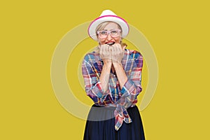 Portrait of sad nervous modern stylish mature woman in casual style with hat and eyeglasses standing, bitting nails and looking at