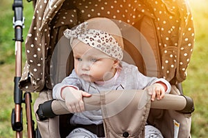 Portrait sad pensive emotional eight-month-old blue-eyes girl sitting in stroller looking away and wait for parent