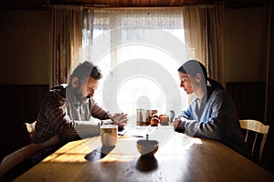 Portrait of sad poor mature couple praying at the table indoors at home, poverty concept.