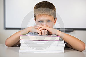 Portrait of sad schoolboy leaning on stack of books in class room