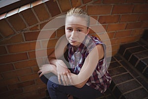 Portrait of sad schoolgirl sitting alone on staircase