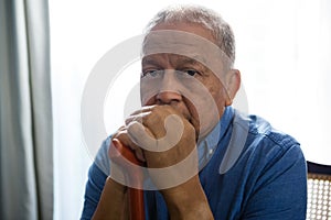 Portrait of sad senior man holding walking cane while sitting on chair