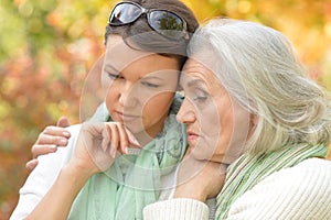 Portrait of sad senior woman with adult daughter in autumnal park