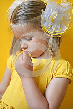 Portrait of sad shy little girl in a yellow dress on a yellow background