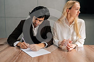 Portrait of sad spouses couple signing decree papers getting divorced in lawyers office at desk. Unhappy married family