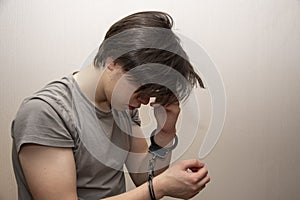 Portrait of a sad teenager in handcuffs on a gray background, medium plan. Juvenile delinquent, criminal liability of minors. photo