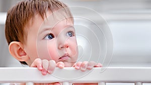 Portrait of a sad toddler baby in a crib. Child face at the bed railing, clo