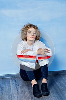 Portrait of a sad transgender guy model with blue eyes and blond hair in the image of a girl on a blue background.