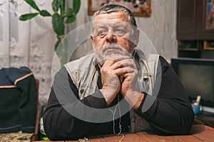 Portrait of sad Ukrainian peasant sitting at wooden table and thinking
