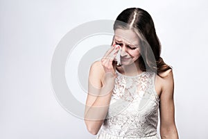 Portrait of sad, unhappy crying woman with freckles and white dress and smart watch on silver gray background.