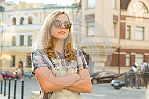 Portrait of sad unhappy teen girl with folded hands on city street, copy space