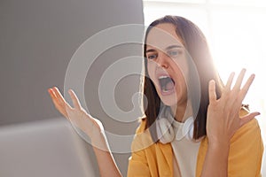 Portrait of sad unhappy woman with brown hair wearing yellow shirt posing in office, having lots of work and troubles with new