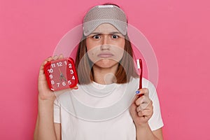 Portrait of sad upset funny woman with blindfold holding red alarm clock and tooth brush, dont like cleaning teeth, looking at