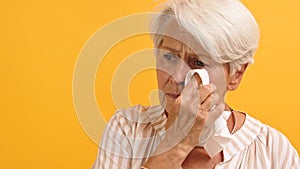 Portrait of sad vulnerable old woman wiping her tears. Isolated on the orange background