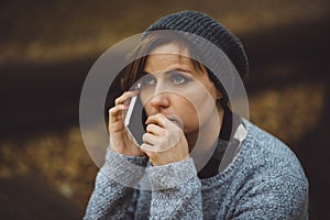 Portrait of sad woman sitting alone in the forest with smartphone. Solitude concept. Millenial dealing with problems and