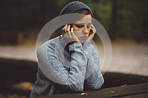 Portrait of sad woman sitting alone in the forest. Solitude concept. Millenial dealing with problems and emotions.