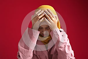 Portrait of sad young Asian muslim girl wearing hijab crying against red background, despression