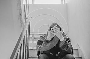 Portrait of sad young man covering his face with hands sitting on old stairs.