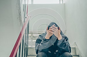 Portrait of sad young man covering his face with hands sitting on old stairs.