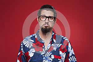 Portrait of a sad young man in Hawaiian shirt against red background.