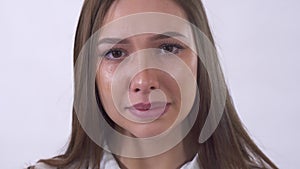 Portrait of sad young woman crying close up on white background in studio. Tear runs down cheek