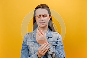 Portrait of sad young woman holding painful hand and grimacing in pain, suffering from trauma or arthritis disease, carpal tunnel